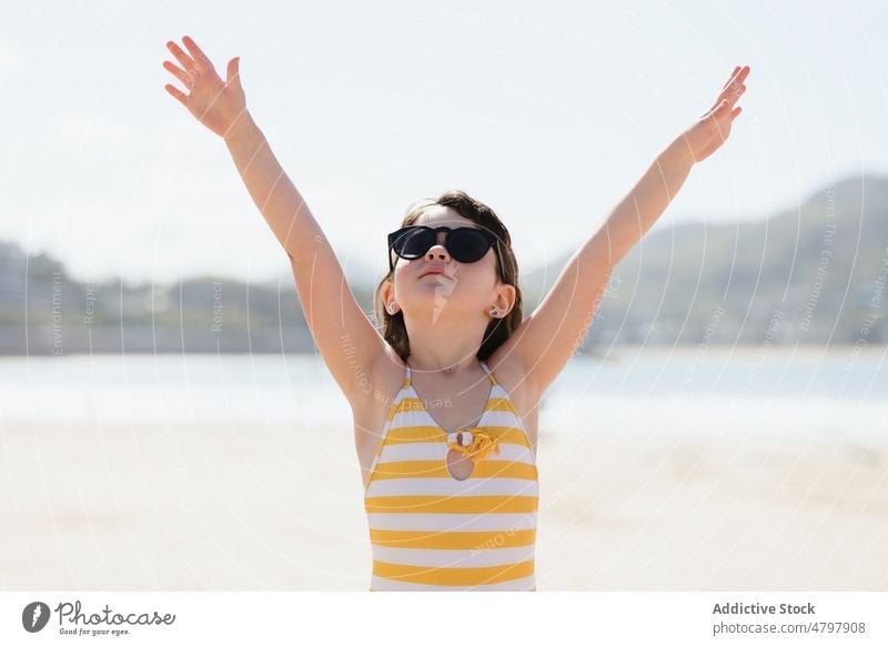 Girl in sunglasses on shore girl kid beach summer coast childhood rest pastime recreation naked torso shirtless arms raised leisure cute swimwear enjoy sand sea