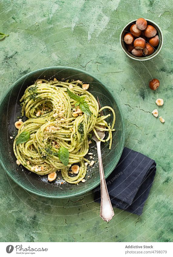 Ceramic plate with hazelnut pesto spaghetti on green table surface bowl rustic dinner culinary basil leaves napkin tagliatelle italy pesto sauce ceramic