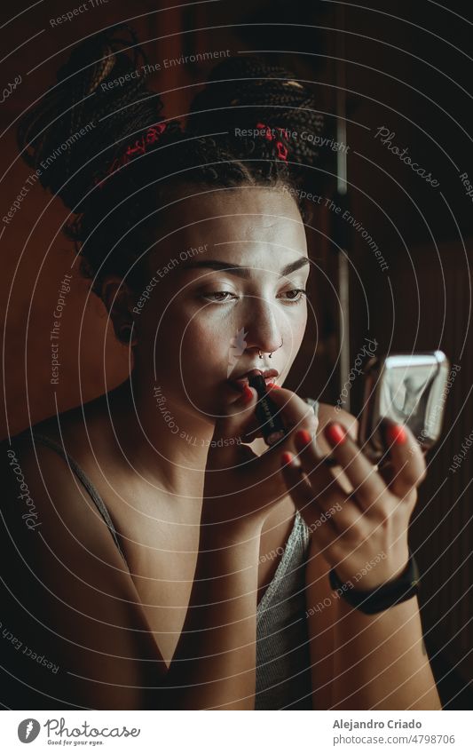 A woman putting on makeup in her room while orange light falls through the window. The woman has braids Brush Glamor care Cosmetics Style Face make-up