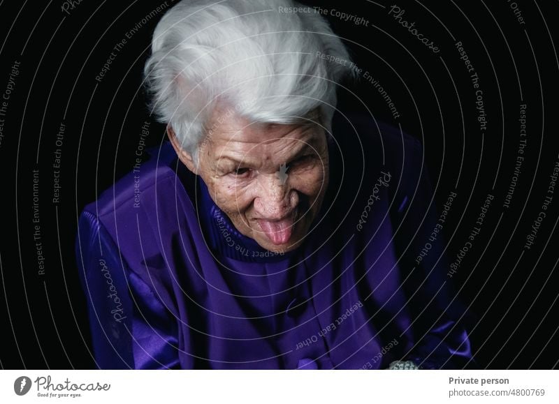 Senior woman, grandmother stuck her tongue out laughs close-up of the face, woman show tongue, portrait with open mouth and protruding tongue.