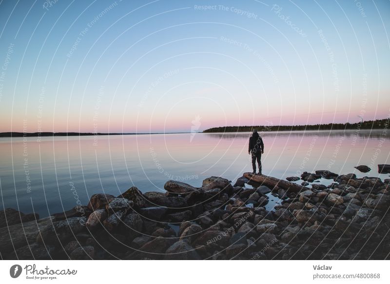 Blue-red-pink frosty sunrise at Lake Oulujarvi near the town of Paltamo in Kainuu region, Finland. An explorer in black dress enjoys the view of the calm surface of Suomi lake