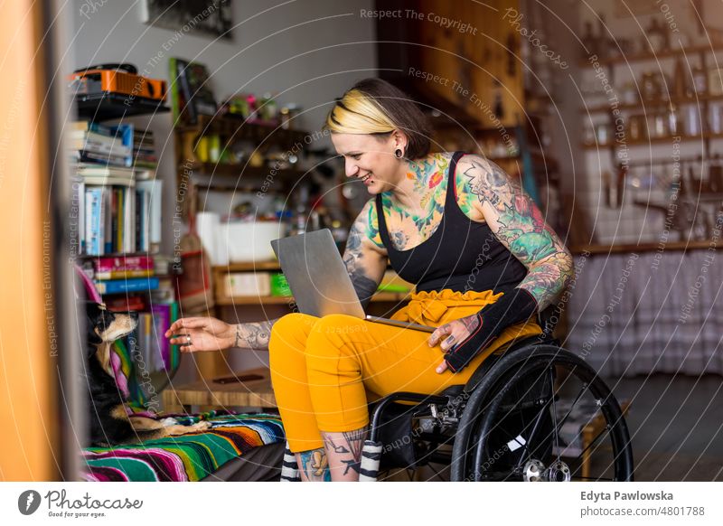 Young tattooed woman in a wheelchair with her dog at home domestic life confidence indoors house people young adult casual female Caucasian attractive beautiful