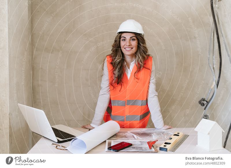 professional confident architect woman in construction site working on blueprints. Home renovation workspace protective helmet protective jacket mobile phone