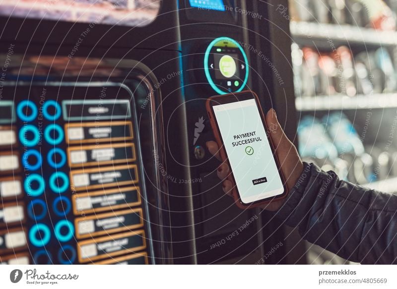 Consumer paying for product at vending machine using contactless method of payment with mobile phone. Woman using payment app on smartphone to buy product