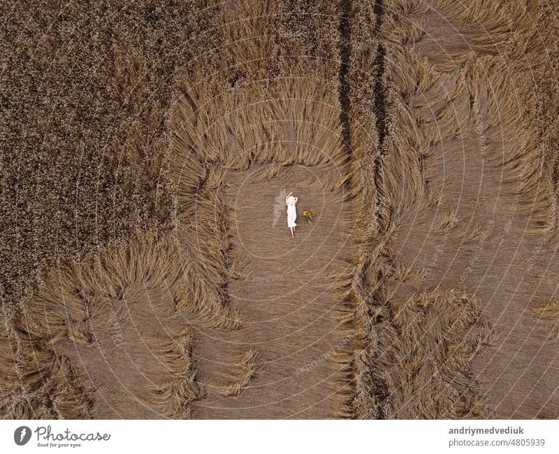 Aerial view of a pretty young woman enjoying the outdoors. girl wearing a white dress lying in wheat field. People, travel, freedom concept. female model nature