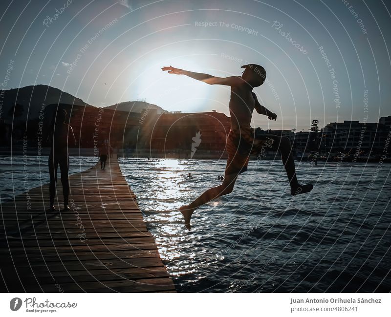 Sunset. Backlit photograph of a child jumping into the sea from a pontoon on a beach on the island of Mallorca, Spain sunset backlit boy pier Majorca spain