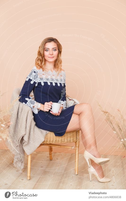 Attractive girl is sitting in a rattan wicker chair with a cup of tea woman armchair indoors coffee jewish lifestyle comfort pastel dead wood house white plaid