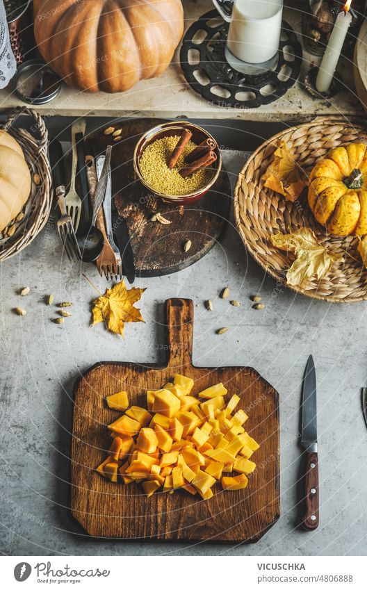 Chopped pumpkin on cutting board on rustic table with cutlery, plates, bowls and kitchen utensils. food background chopped cooking home seasonal autumn