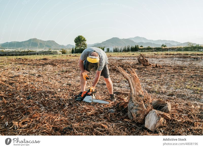 Anonymous farmer cutting firewood with chainsaw in countryside field prepare man trunk male tree mountain nature highland rural equipment tool instrument modern