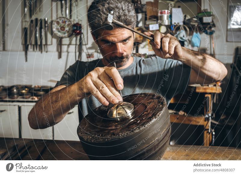 Focused silversmith punching ornament on silver lid man carve hammer table workshop male mature middle age create artisan hit handmade skill manufacture