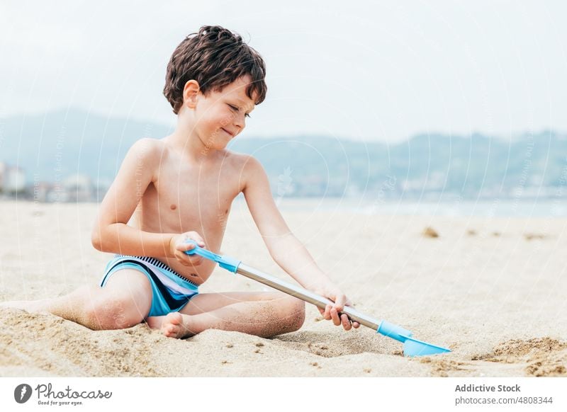 Glad little boy digging sand on beach summer vacation smile shovel weekend glad child coast relax shore kneel childhood rest resort happy kid holiday cheerful