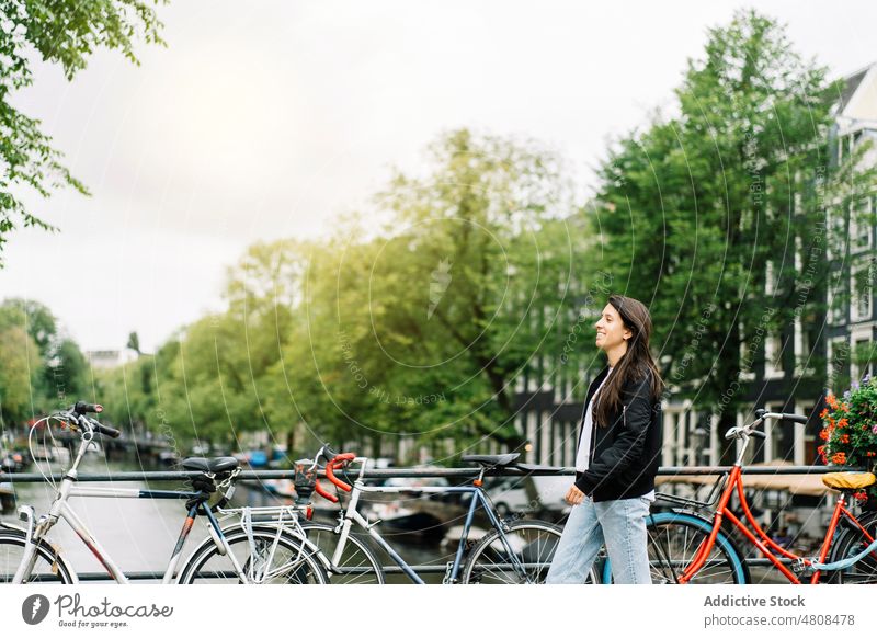 Happy ethnic woman smiling while standing on footbridge on cloudy day smile city canal bicycle traveler happy style holiday trip vacation female young hispanic