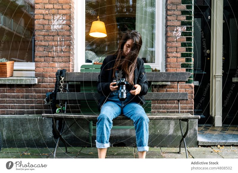 Serious young ethnic lady with photo camera sitting on bench on city street woman photographer photography check traveler building trip female style hispanic