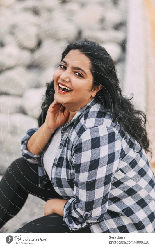 Street portrait of an Indian girl in a plaid shirt outdoors young beautiful indian sitting smiling street style asian woman fashion trendy fashionable