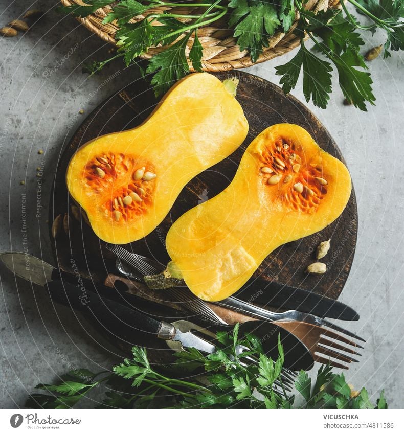 Pumpkin halves on round wooden cutting board with cutlery on grey kitchen table with herbs. pumpkin cooking preparation home seasonal autumn squash