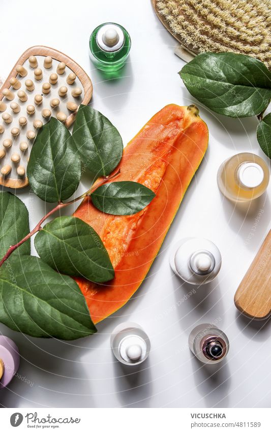 Body care setting with papaya half, massage brushes, cosmetic products and green leaves on white background. Modern spa and wellness body care