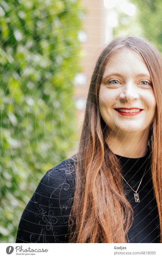 Young woman with long hair and black clothes smiles at camera in front of green ivy Woman Smiling portrait Feminine pretty Face 18 - 30 years Adults Human being