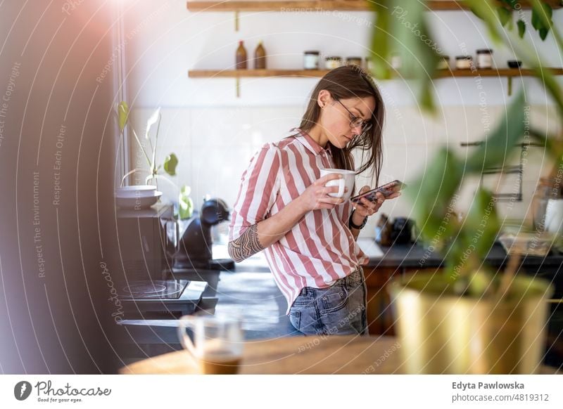 Young woman using smartphone while standing in her kitchen at home mobile phone technology online internet using phone communication domestic life confidence