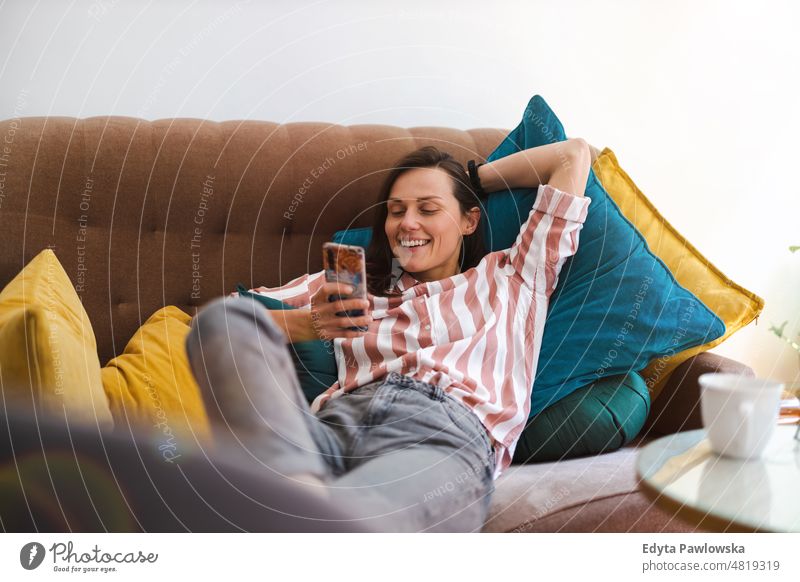 Happy young woman using mobile phone on sofa smartphone technology online internet using phone communication domestic life confidence indoors home house people