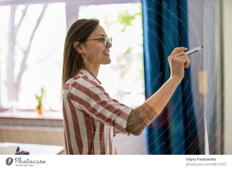 Young woman writing with a marker on white board in the office domestic life confidence indoors home house people young adult casual female Caucasian attractive