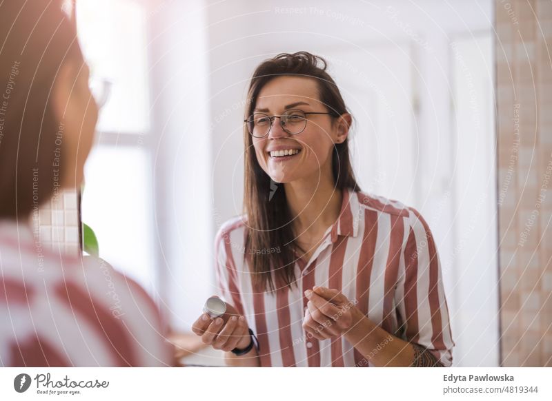 Young woman looking in bathroom mirror domestic life confidence indoors home house people young adult casual female Caucasian attractive beautiful tattoos one