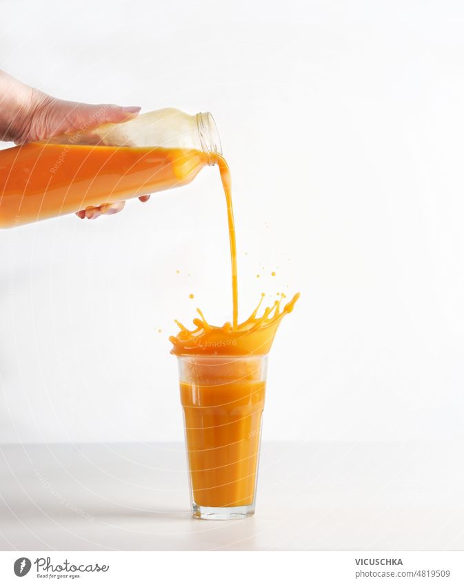 Women hand pouring homemade yellow juice from bottle in glass with splashing liquid at white background. women prepared healthy smoothie drink front view motion