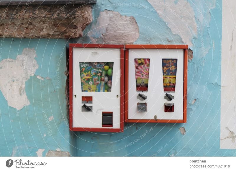 Two vending machines, gumball machines on a light blue house wall with peeling plaster Nostalgia Gumball machine Plaster Infancy Chewing gum Candy Retro Toys