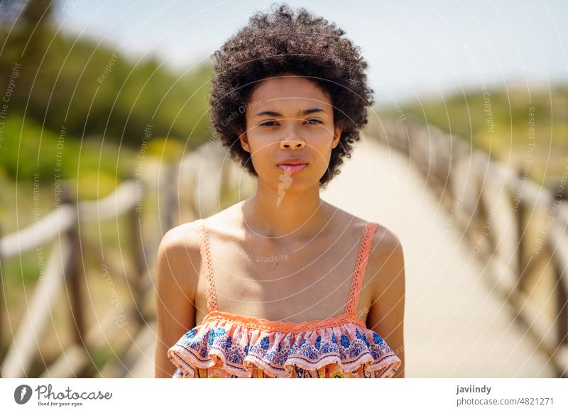 Young black woman, with afro hair, on a wooden path on the dunes of a tropical beach. summer nature face curly hairstyle female beauty model attractive portrait