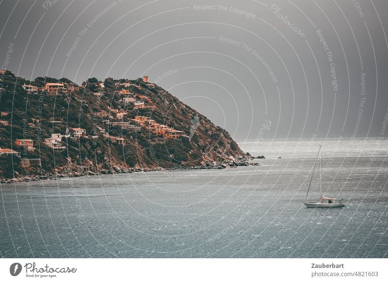 Sailing yacht is anchored against gloomy sky in a bay in Sardinia, in the background hills and vacation houses sailing yacht Sailboat Anchor Drop anchor Bay