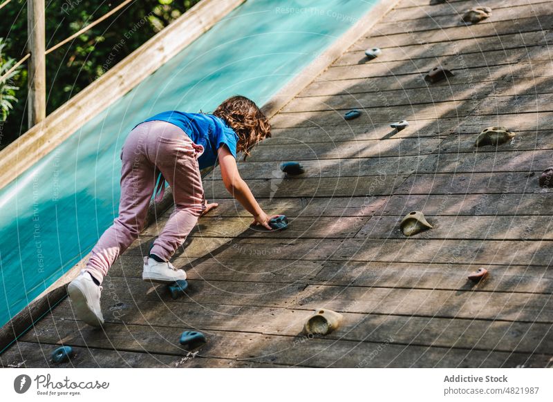 Anonymous child practicing climbing on wall on playground girl park boulder training activity practice hobby extreme active childhood exercise nature kid casual