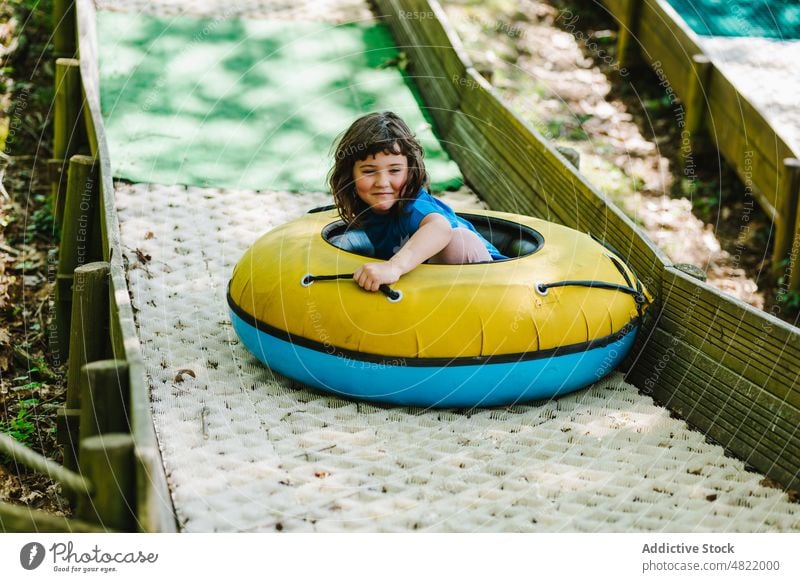 Happy little girl riding inflatable sledge on ramp in park child ride slide tube activity playground cheerful smile happy portrait summer entertain joy kid