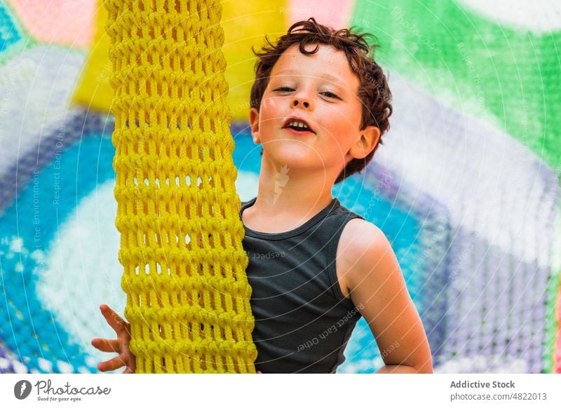 Content little kid playing on knitted trampoline on playground child smile happy cheerful entertain boy childhood joy portrait center positive colorful adorable