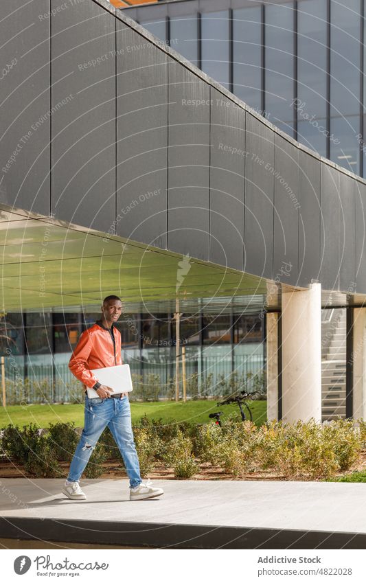 African American guy with laptop walking along park after working day man campus student freelance university path remote confident trendy self employed