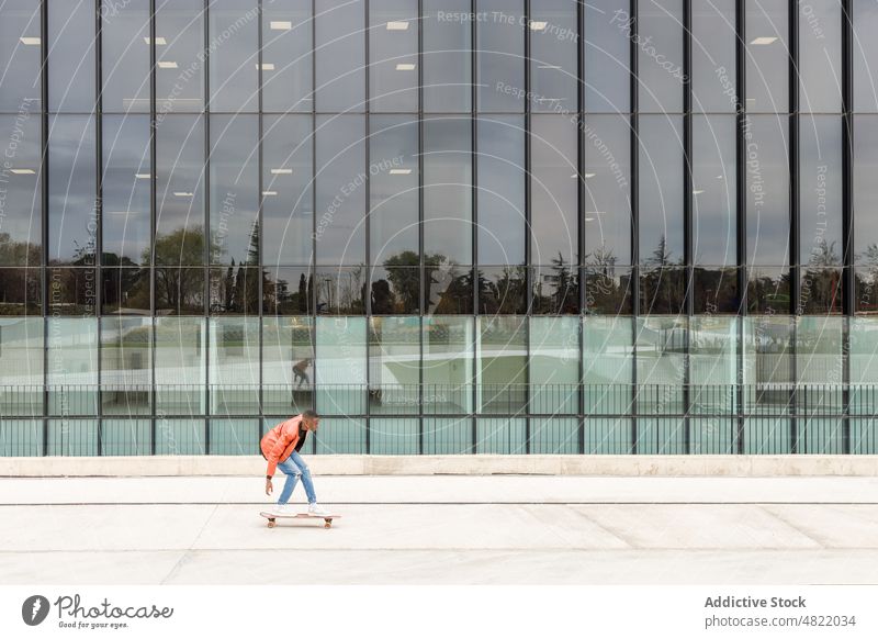 Cool young black man riding skateboard on modern city street ride building trendy cool skater activity style confident millennial male african american ethnic