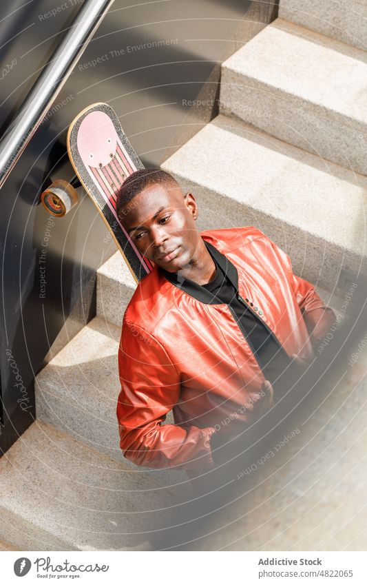 Tranquil African American guy leaning on skateboard on street stairs man relax staircase trendy cool skater free time rest student looking away generation z