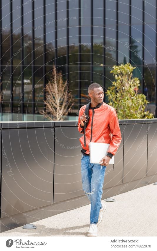 Confident black male student strolling near modern building in city man walk street backpack laptop confident serious trendy urban generation z contemporary