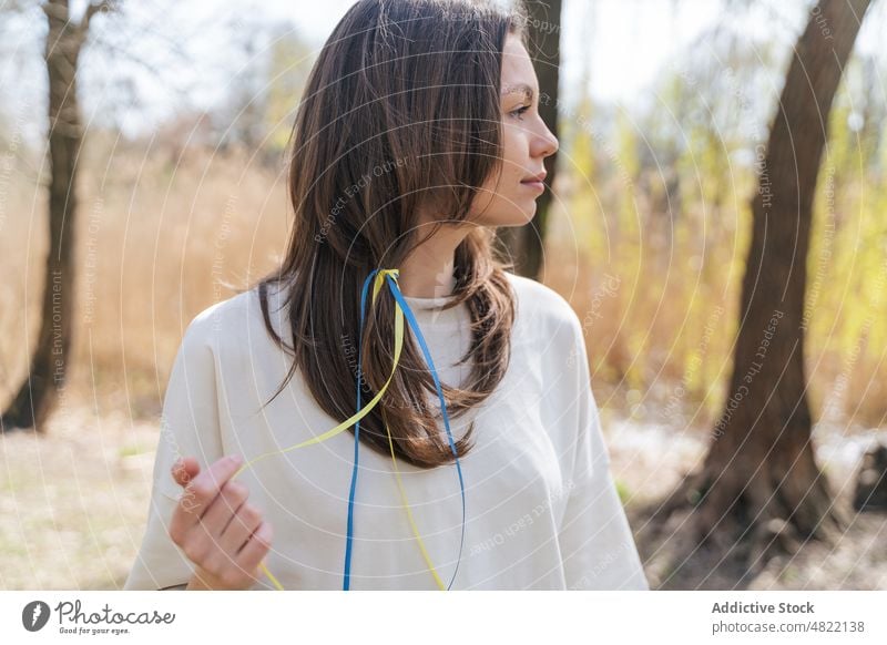 Lady with blue and yellow ribbons in hair standing in nature woman ukrainian flag smile calm patriot portrait feminine field sunlight peace female young