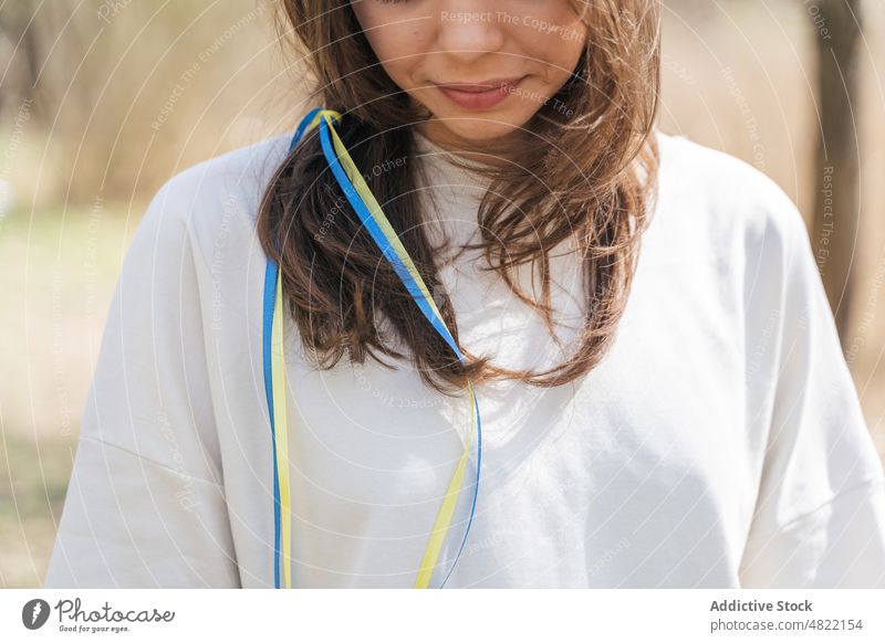 Smiling lady with blue and yellow ribbons in hair standing in nature woman ukrainian flag smile calm patriot portrait feminine field sunlight peace female young