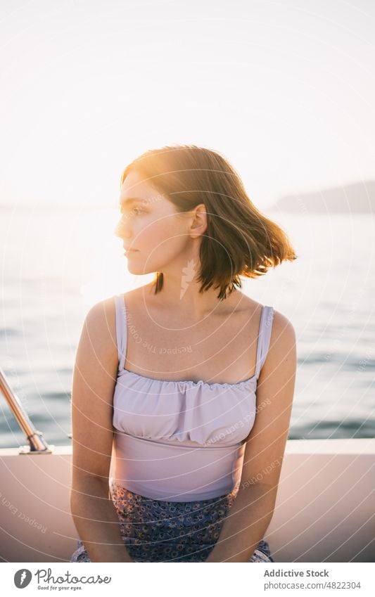 Calm young lady admiring nature while sitting on sailboat woman sea yacht admire holiday cruise summer vacation female portrait trendy style trip brown hair