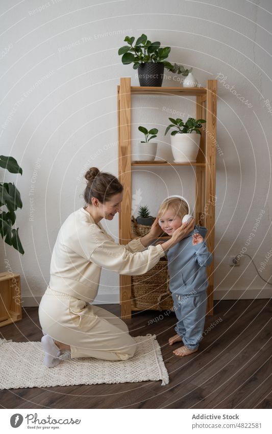 Smiling mom adjusting headphones of adorable little son woman child put on listen music smile cheerful mother together happy home female kid casual young boy