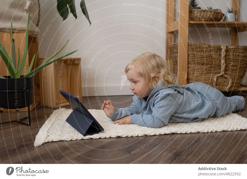 Cute toddler lying on floor and watching video on tablet child curious interest attentive cartoon internet interesting apartment casual blond childhood online