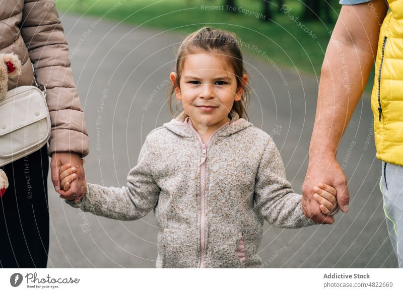 Cheerful little kid holding hands of grandparents in park child walk happy spend time together granddaughter relationship cheerful joy raise girl casual mature