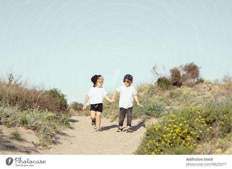 Happy little siblings holding hands while strolling on beach children walk path together happy trendy brother holiday plant cheerful kid toddler blond style