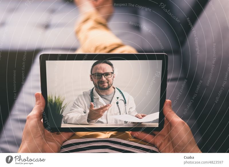 Woman lying on a sofa and talking with a doctor online using digital tablet. Telemedicine concept. telemedicine technology woman patient unrecognizable health