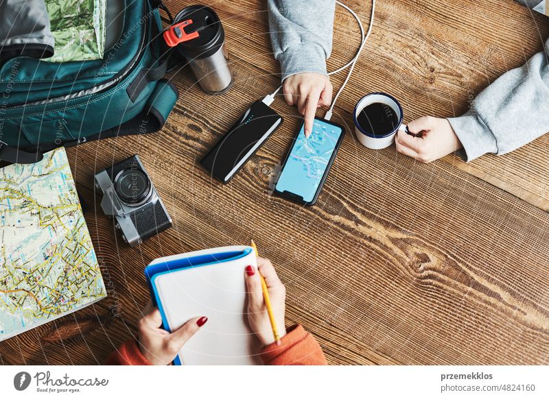 Family planning vacation trip. Girl searching travel destination and routes using navigation map on mobile phone. Charging smartphone with power bank. Using technology while travelling