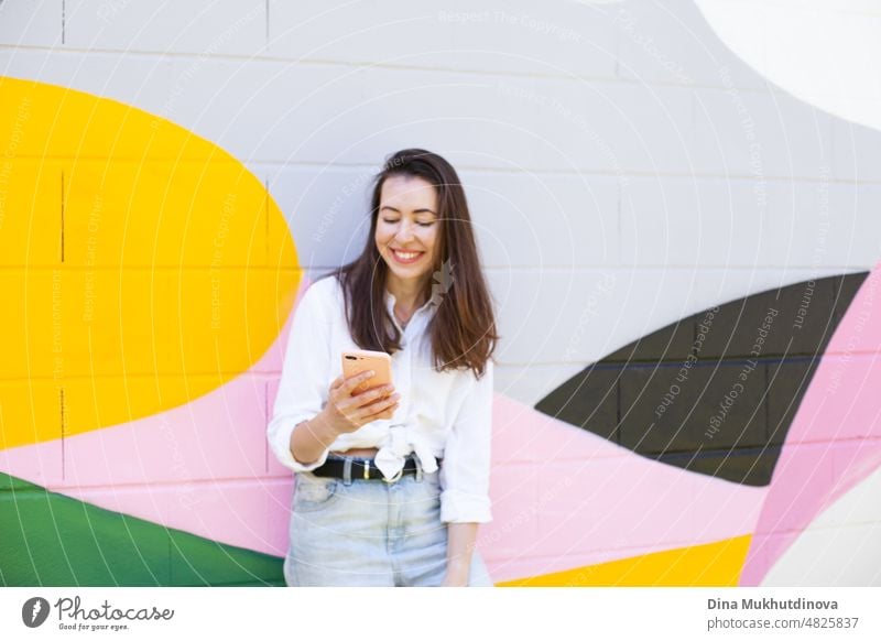 Young woman holding a mobile phone and video chatting standing near vibrant colorful wall in the city. Happy woman smiling and using technology. beautiful