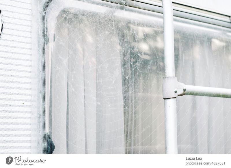 Behind the window of a disused mobile home still hangs a delicate white curtain, in front of it a large spider web Mobile home Caravan decommissioned Old