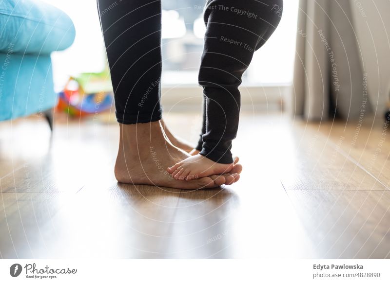 Baby son standing on mothers feet walking active adult affection baby barefoot bonding boy candid care casual cheerful child childhood closeup cute enjoying