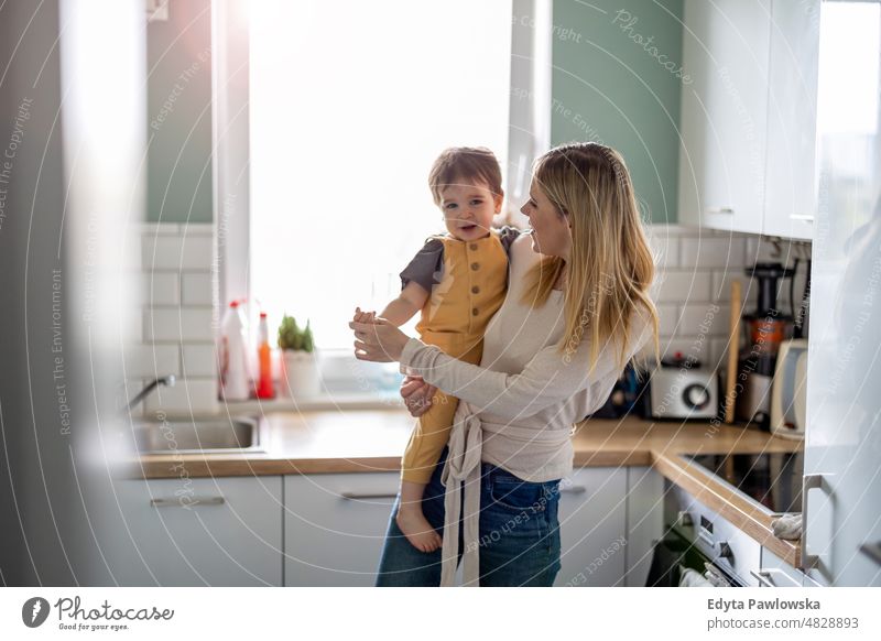 Young mother with child in the kitchen adult affection baby bonding boy candid care childhood domestic enjoying family fun happiness happy home house indoors