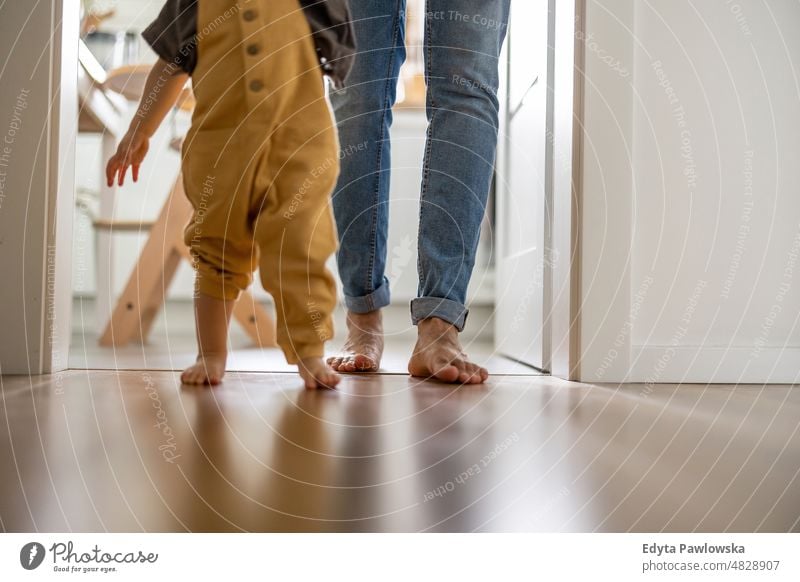 Little baby boy learning to walk with his father beside him at home walking standing active adult affection barefoot bonding candid care casual cheerful child